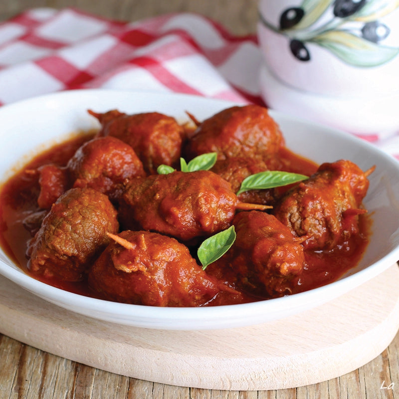 Bowl of beef involtini in red sauce with basil leaves on a checkered tablecloth.