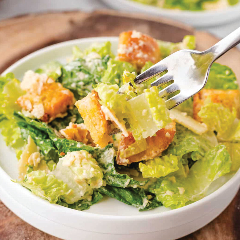 Italian Catering Caesar salad with croutons and a fork in a white bowl on a wooden surface