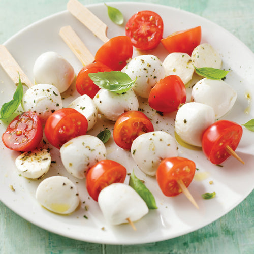 Caprese salad skewers on a white plate with a green background