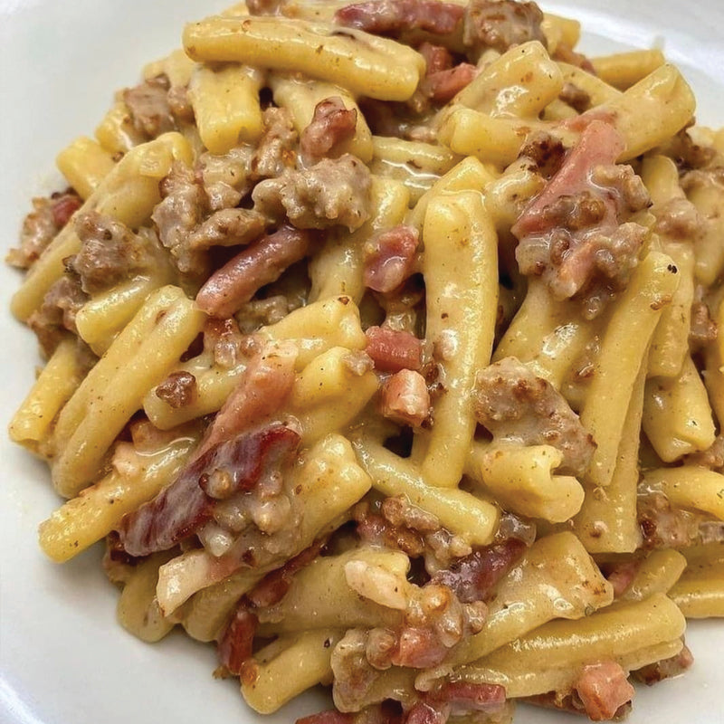 Pasta dish with ground meat and bacon on a white plate
