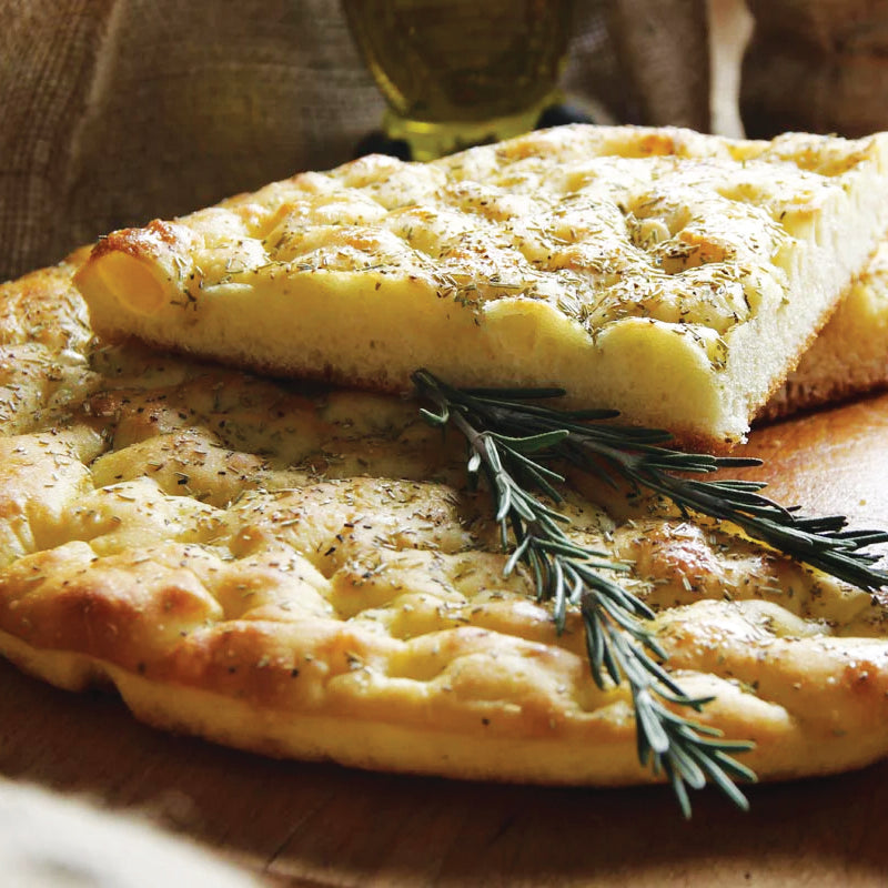 Focaccia bread with a slice cut out, garnished with rosemary on a wooden board.