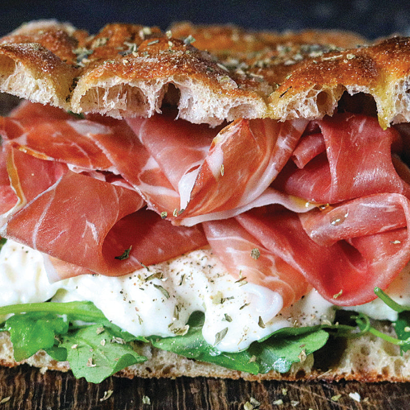 Italian Catering focaccia with prosciutto, mozzarella, and lettuce on a wooden surface