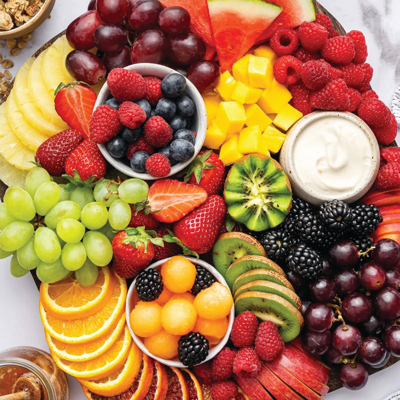 Assorted fruits including strawberries, grapes, kiwi, and melons arranged on a platter with a small bowl of blueberries.