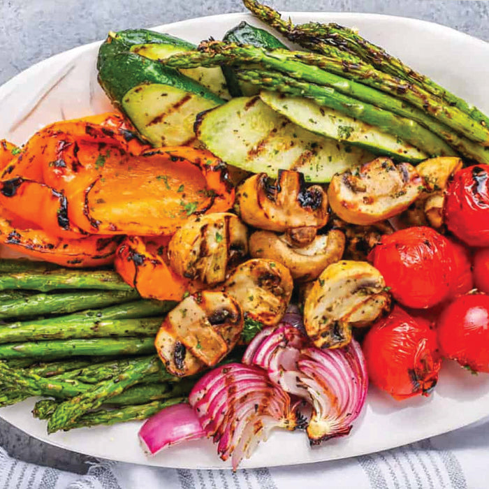 Platter of grilled vegetables including asparagus, zucchini, carrots, mushrooms, and cherry tomatoes on a white plate.