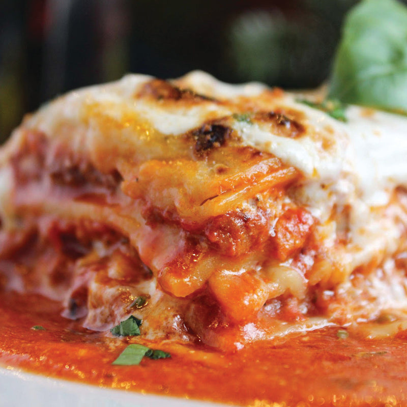 Close-up of a slice of lasagna with tomato sauce and melted cheese on a wooden board.