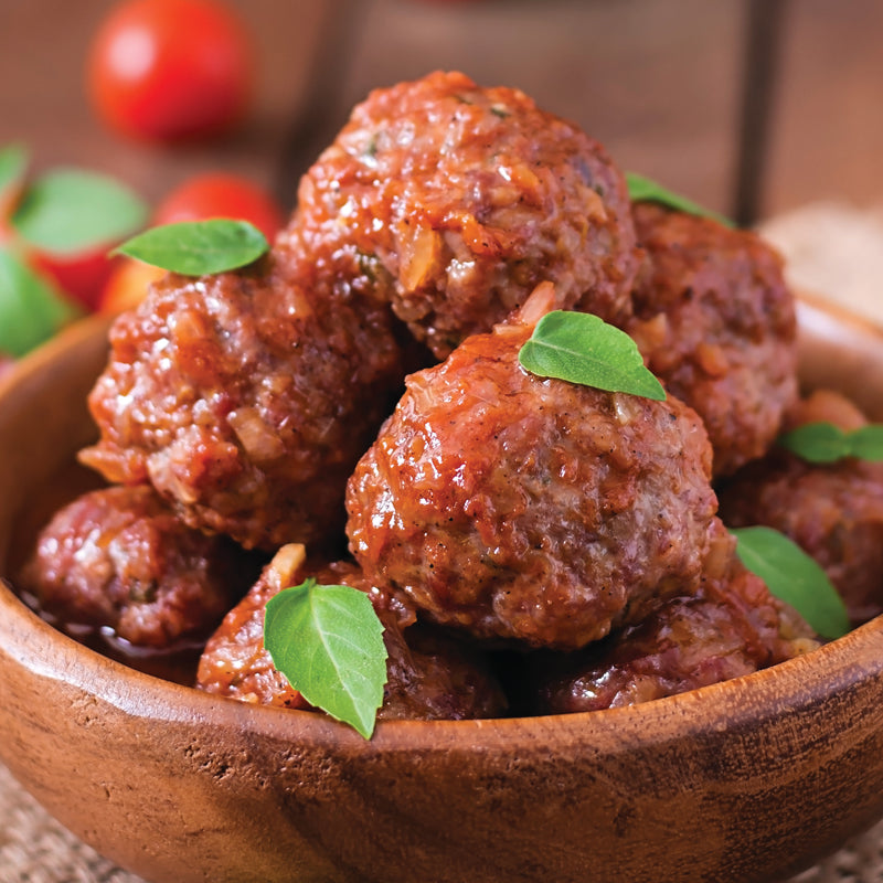Wooden bowl filled with meatballs garnished with green leaves on a wooden surface.