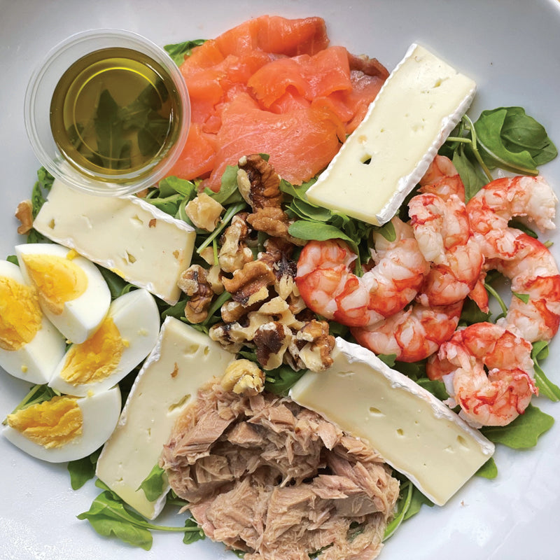 Italian Catering ocean salad with shrimp, eggs, cheese, walnuts, smoked salmon and other ingredients on a white plate.