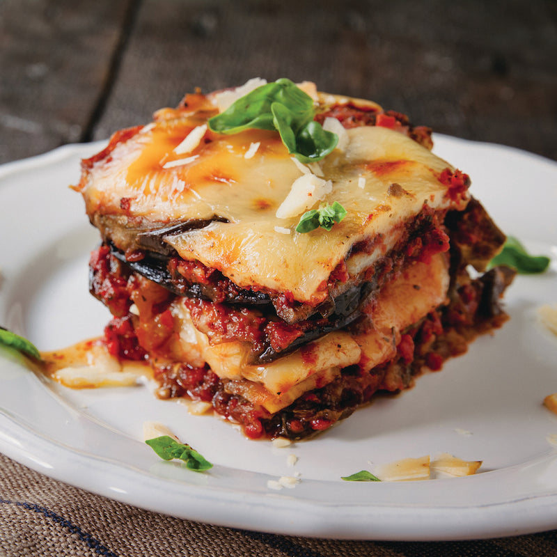 Slice of eggplant parm on a white plate with basil leaves