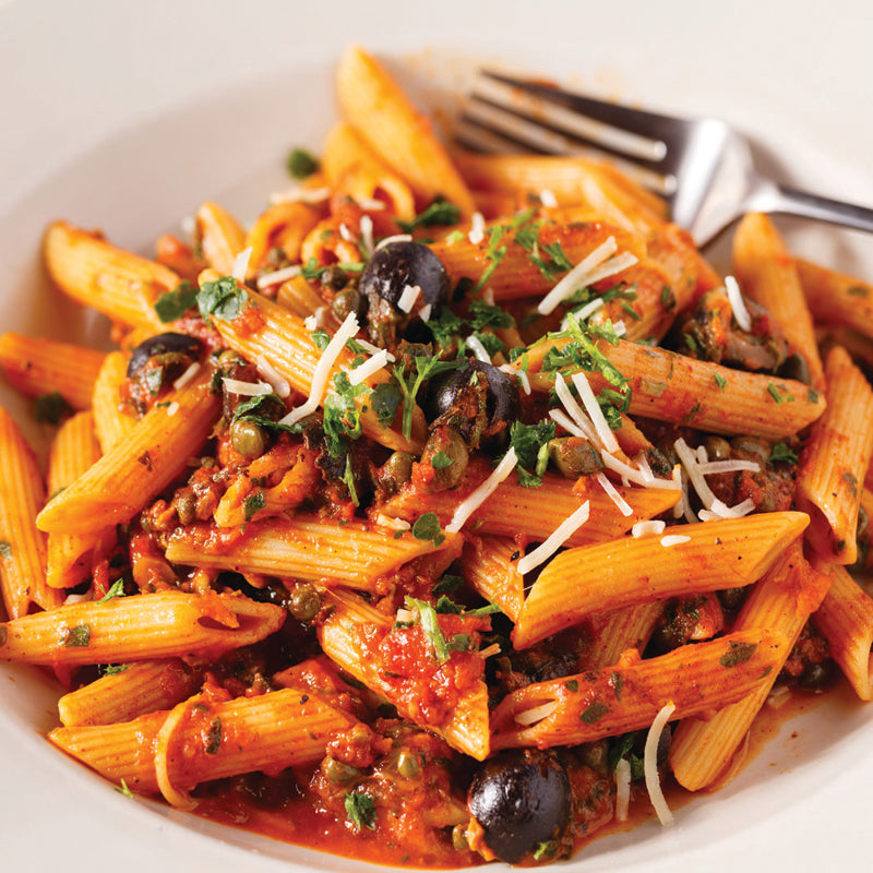 Penne pasta puttanesca with tomato sauce, olives, and herbs on a white plate with a fork.