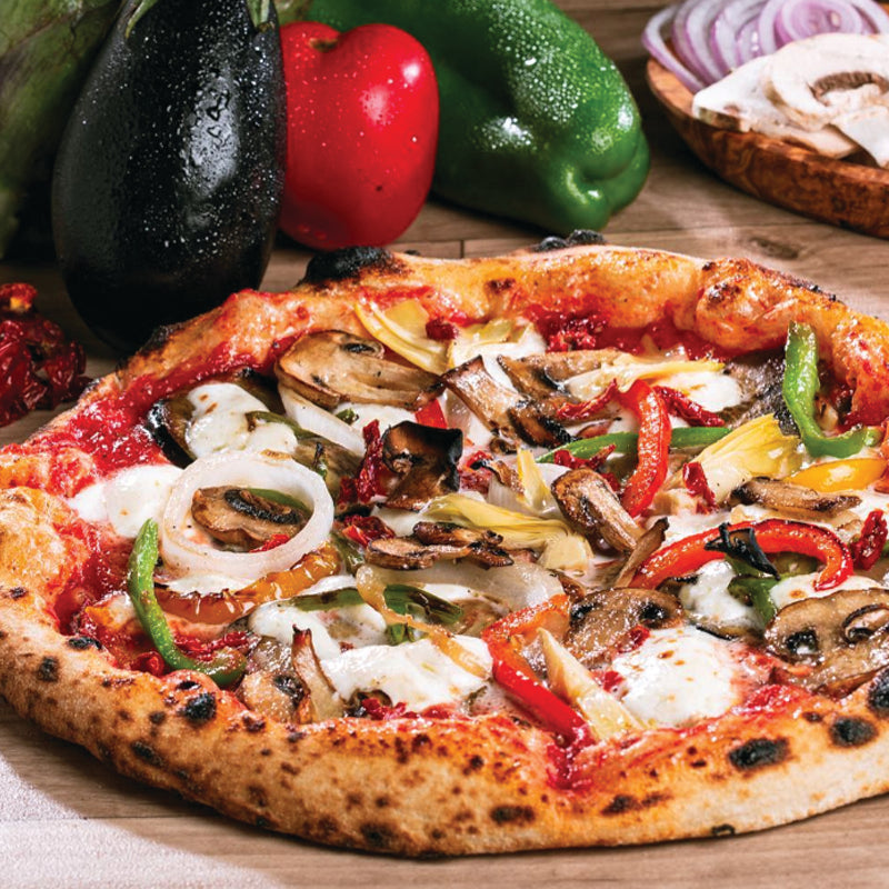 Vegetable pizza with various toppings on a wooden board, surrounded by fresh vegetables.
