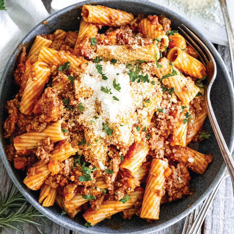 Pasta dish with ground meat, parmesan cheese, and herbs in a bowl.