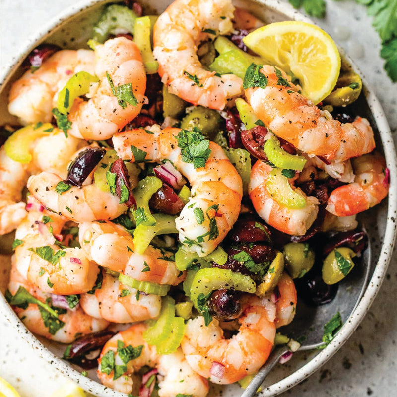 Shrimp salad with olives, celery, and lemon wedges in a bowl.