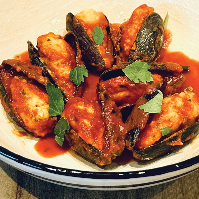 Mussels in a red sauce on a white plate with a blue rim