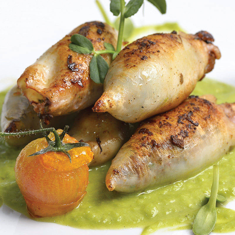 Grilled squid with a green sauce and cherry tomato on a white plate