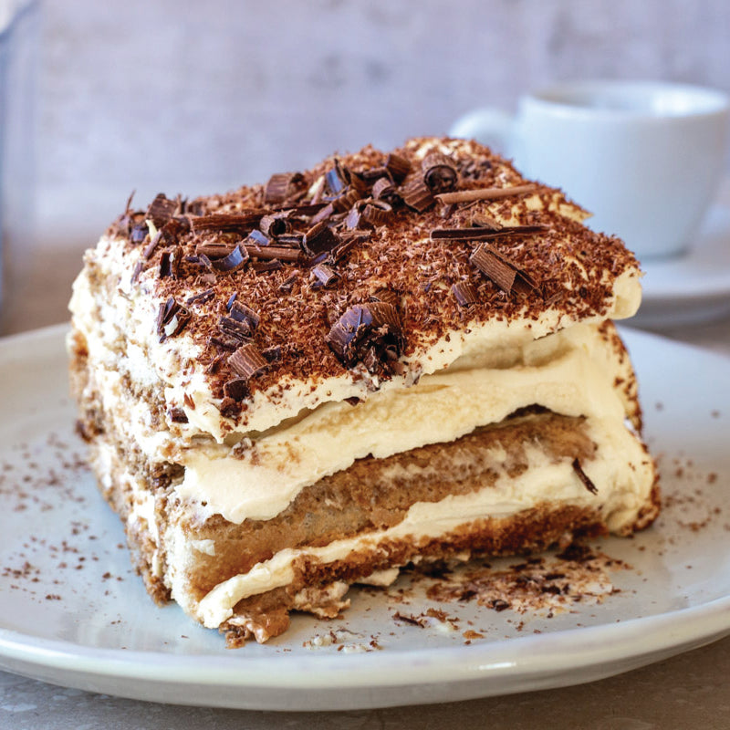 Slice of tiramisu' layered dessert with chocolate shavings on a white plate